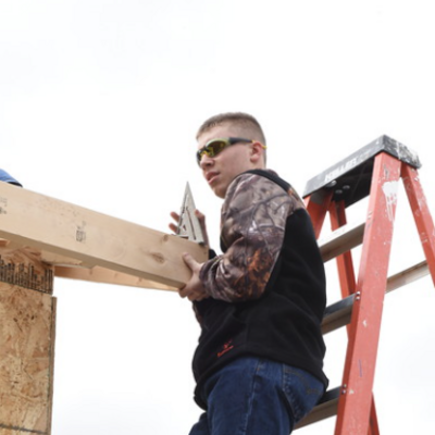 Student on ladder measuring pitch of a roof.