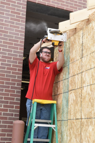 Student sawing off rafters on a small shed being built.