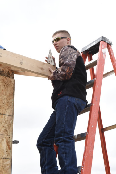 Student on ladder measuring pitch of a roof.